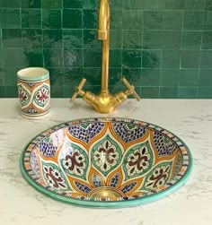 a bathroom sink with an ornate design on the bowl and gold faucet next to it