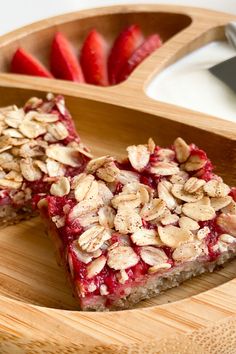 two slices of strawberry crumble bars on a wooden tray with strawberries in the background