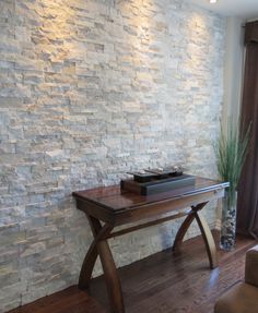 a living room with a couch, table and chair next to a stone brick wall