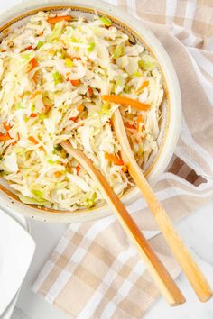 a white bowl filled with coleslaw next to two wooden spoons on top of a table