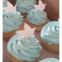 cupcakes with blue frosting and white dove decorations on top in a box