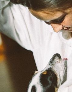 a woman in white shirt petting a black and white dog with his nose open