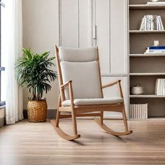 a rocking chair sitting in front of a book shelf filled with books and a potted plant