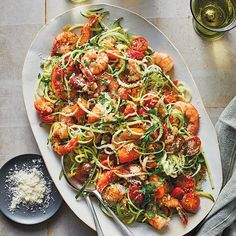 a white plate topped with zucchini noodles and shrimp next to a glass of wine