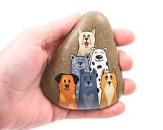 a hand holding a rock with dogs painted on it's face and the rocks are in different colors