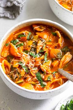 two bowls filled with pasta and vegetable soup on top of a white table next to another bowl