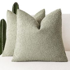 two green pillows sitting next to each other on a white couch with a cactus in the background