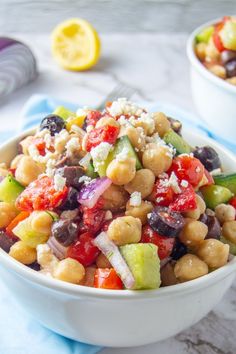 a salad with chickpeas, tomatoes, cucumbers and olives in a white bowl