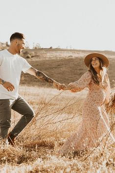 a man and woman holding hands while walking through tall grass in an open field together