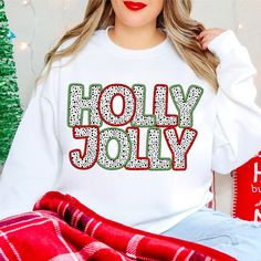 a woman wearing a white sweatshirt with the words holly jolly on it in red and green