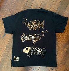 a black t - shirt with gold fish and skeleton bones on the front, sitting on a wooden floor