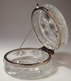 an ornate glass box with a chain hanging from it's lid, on a white surface