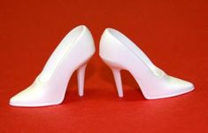 pair of white high heeled shoes on red surface with one shoe facing the other