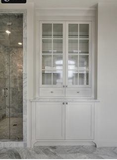 a walk in shower sitting next to a white cabinet and glass doored cupboards