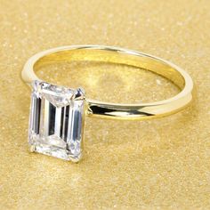 an emerald - cut diamond ring sits on a gold background