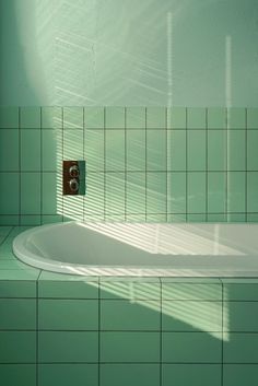 a bathtub in a green tiled bathroom with the sun shining on it's wall