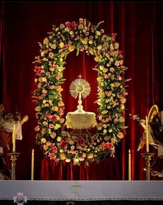 the altar is decorated with flowers, candles and an angel in front of red curtains