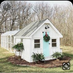 a small white shed with a blue door and wreath on it's front window