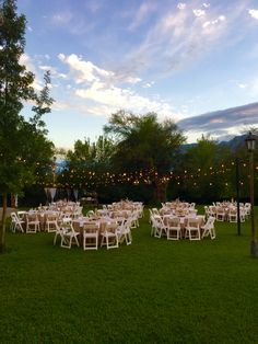 tables and chairs are set up on the lawn for an outdoor wedding reception at dusk