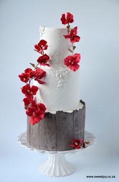 a three tiered white cake with red flowers on the top and bottom, sitting on a wooden stand