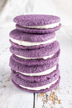 a stack of purple cookies sitting on top of a white wooden table covered in frosting