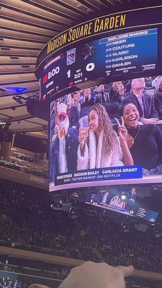 a large screen in the center of a sports arena with people watching and talking on their cell phones