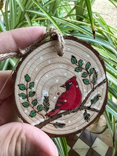 a hand holding a wooden ornament with a cardinal on it