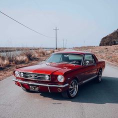 an old red car is parked on the side of the road in front of some dry grass