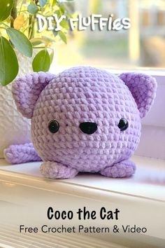 a purple crochet cat sitting on top of a window sill next to a potted plant