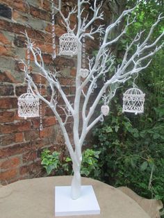 a white tree with birdcages hanging from it's branches in front of a brick wall