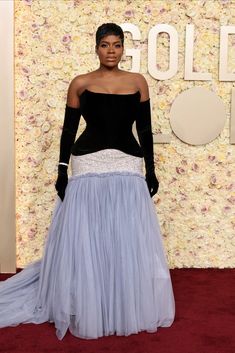 a woman in a blue and white dress standing on a red carpet with flowers behind her