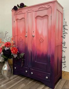 a pink and purple painted armoire next to a vase with flowers