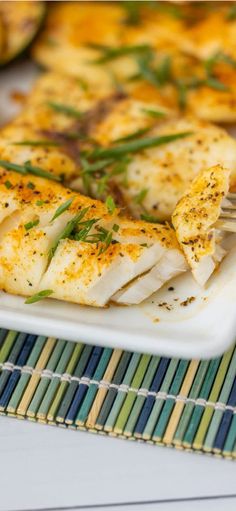 a white plate topped with fish next to potatoes and green garnish on a bamboo mat