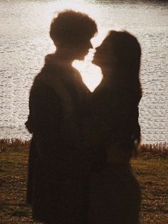 two people standing next to each other in front of a body of water at sunset