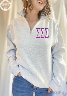 a woman wearing a gray sweatshirt with purple letters on the front and bottom, smiling at the camera