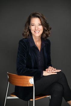 a woman sitting in a chair with her arms crossed and legs crossed, smiling at the camera