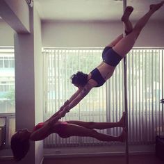 two women doing acrobatic tricks on a pole in a room with blinds