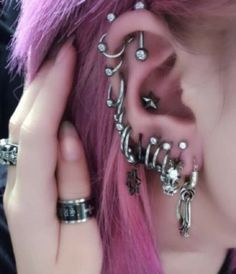 a close up of a person with pink hair and piercings on her ear wearing rings