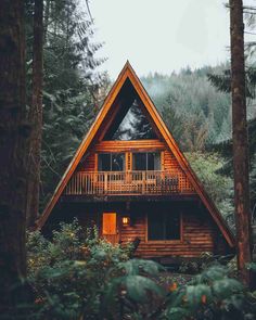 a - frame cabin nestled in the woods surrounded by tall pine trees and greenery