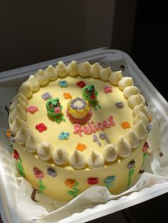 a birthday cake with white frosting and colorful decorations on the top sits in a plastic container