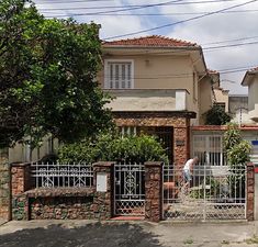 a man is walking down the street in front of some houses with gates and trees