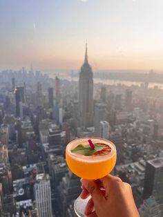 a person holding up a drink in front of a cityscape