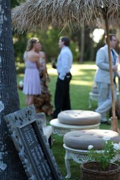 a group of people standing around an outdoor area with furniture and umbrellas on the grass