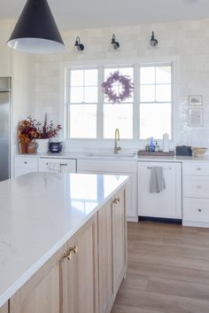 a kitchen with white cabinets and an island in front of a window that has wreaths on it