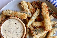 a white plate topped with fried asparagus next to a dipping sauce