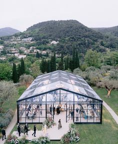 an aerial view of a glass house in the middle of a field with people walking around