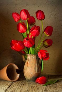 a vase filled with red flowers on top of a wooden table next to a clay jug