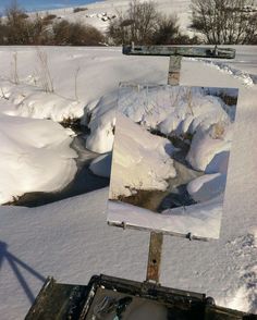 an artist's easel is covered in snow and has a painting on it