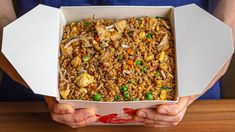 a person holding a box filled with rice and vegetables