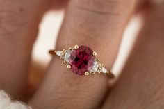 a woman's hand holding a ring with a red and white stone in it